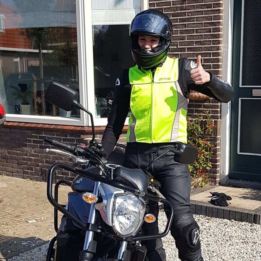 Motorleerling in een geel hesje steekt zijn duim op